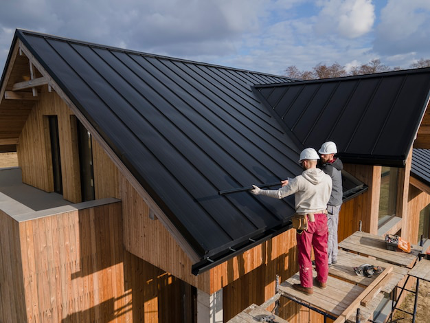 Full shot of roofers working together on a roof, all wearing helmets for safety.