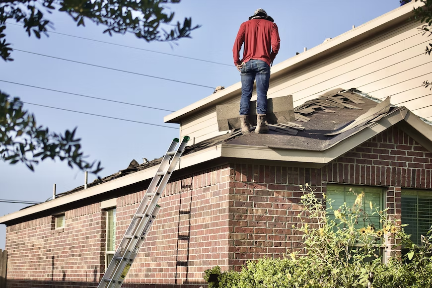 A roof contractor on the roof of a home, inspecting the roofing