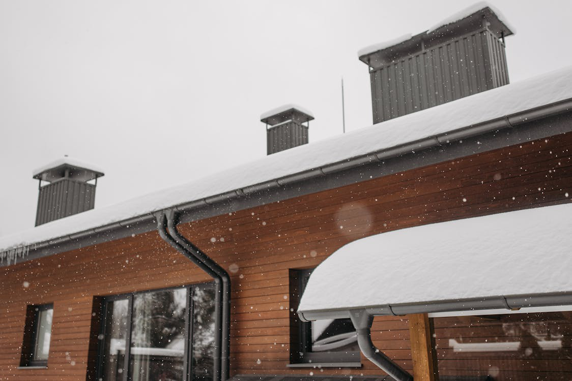 A snow-covered roof featuring chimneys, emphasizing the need for professional chimney services during harsh winters.