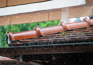 A house roof during heavy rain with water flowing through a properly installed gutter system.